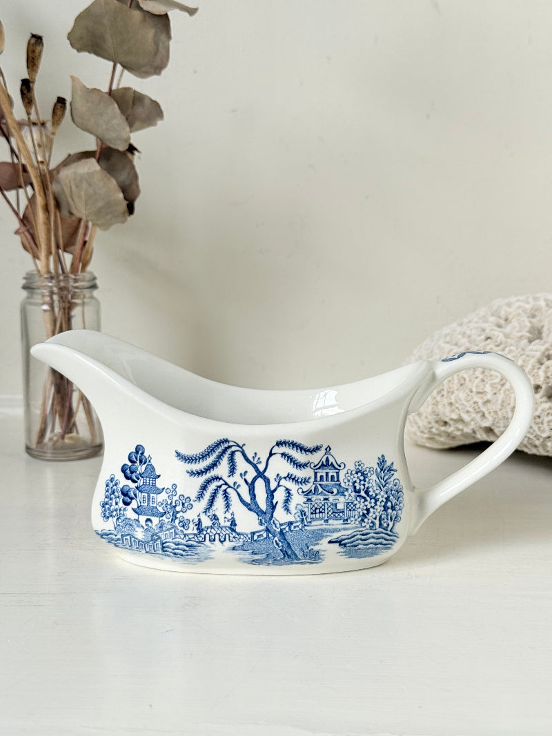 Vintage blue and white ceramic sauce boat with willow pattern photographed on a white surface
