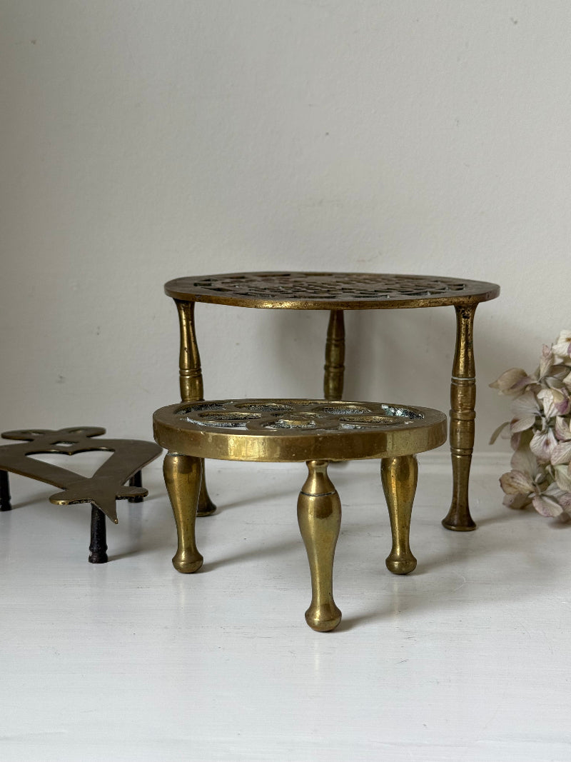 Vintage brass trivet trio with ornate cutwork designs and aged patina, photographed on a white surface