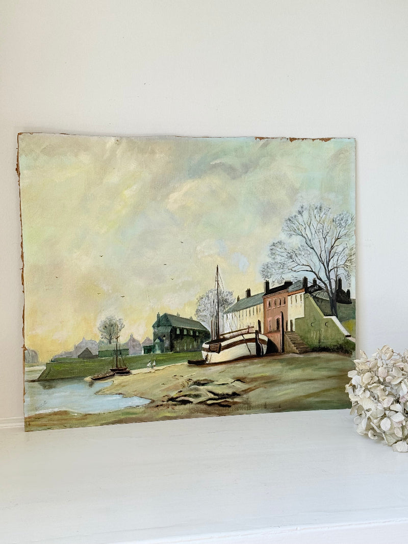 Vintage oil painting on board of a rural village scene with houses, trees, and water, photographed on a white surface