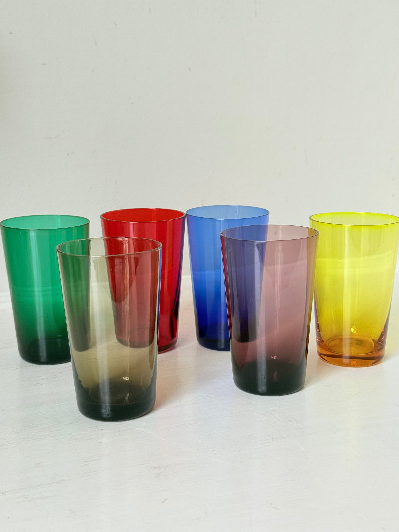 Set of six mid-20th century Boussu coloured glass beakers in rainbow hues, green with original label, photographed on white surface.