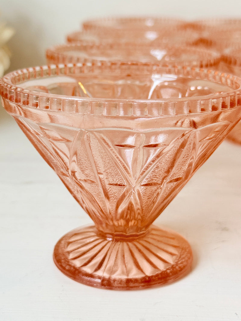 A close-up of a pink cut-glass dessert bowl with a flared base, shown with several matching bowls blurred in the background on a light surface.