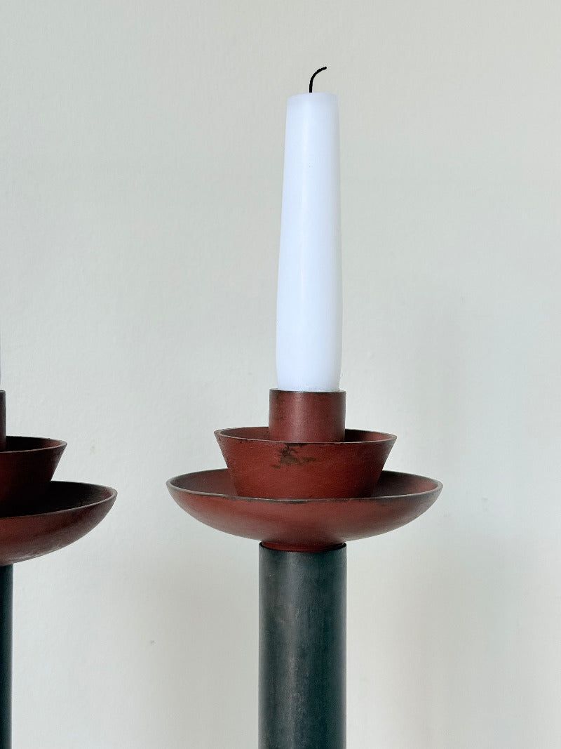 Pair of tall vintage metal candlesticks in black and burgundy, styled with white taper candles on a white surface.