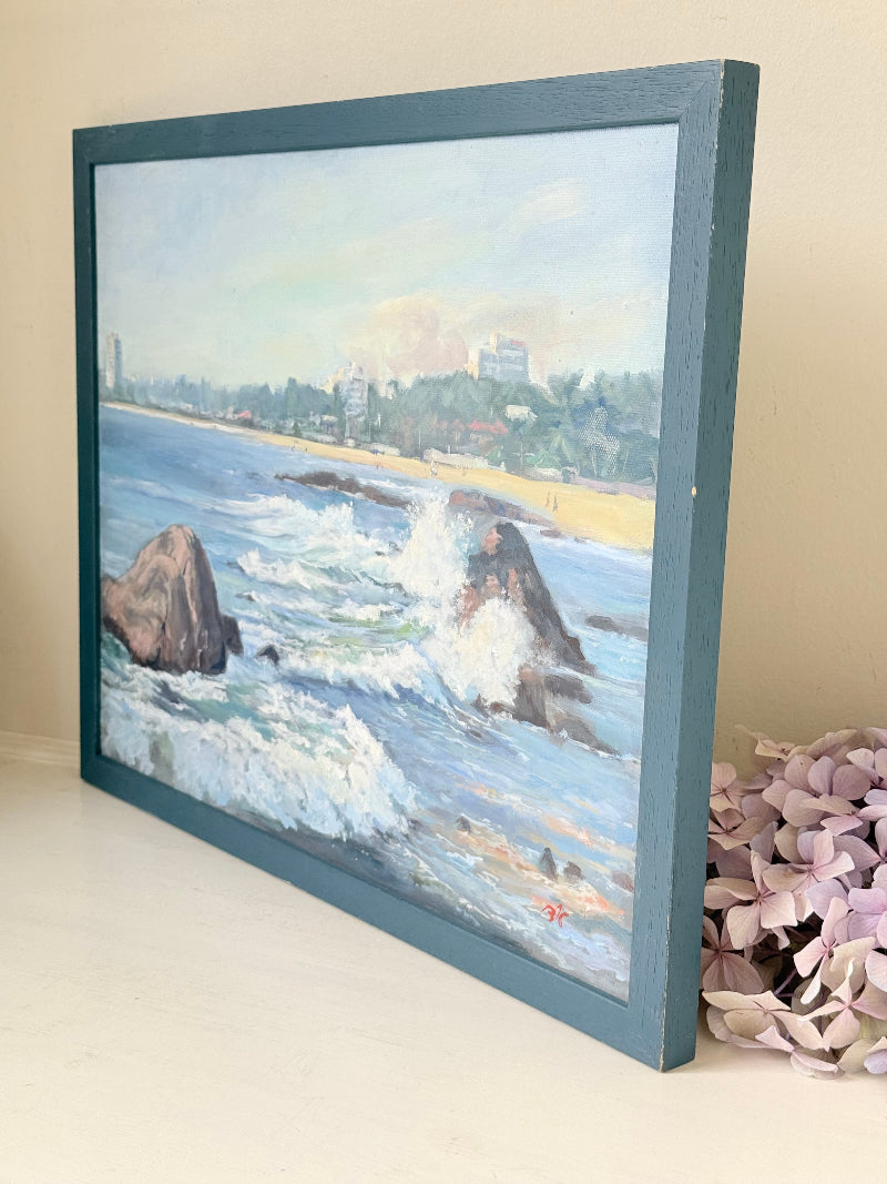 Original oil painting of waves crashing against rocks, signed seascape in slate blue wooden frame on white surface