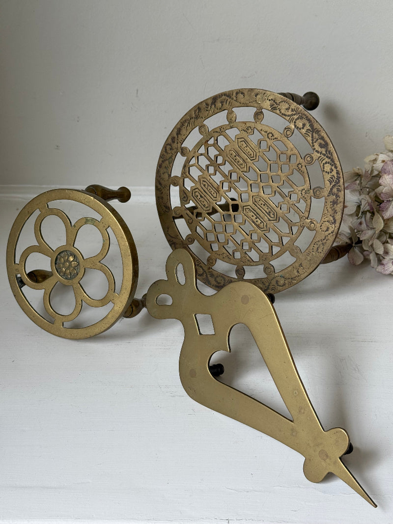 Vintage brass trivet trio with ornate cutwork designs and aged patina, photographed on a white surface