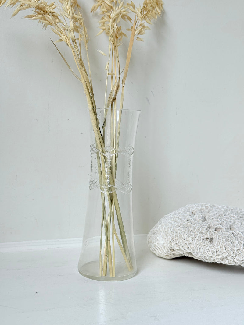 Vintage clear glass cylinder vase with etched leaf design, photographed on a white surface.