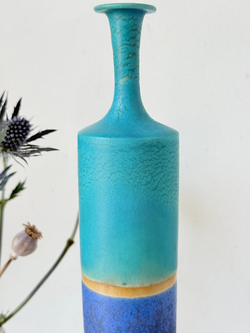 Tall vintage studio pottery bottle vase in turquoise and cobalt blue glaze, photographed on a white surface
