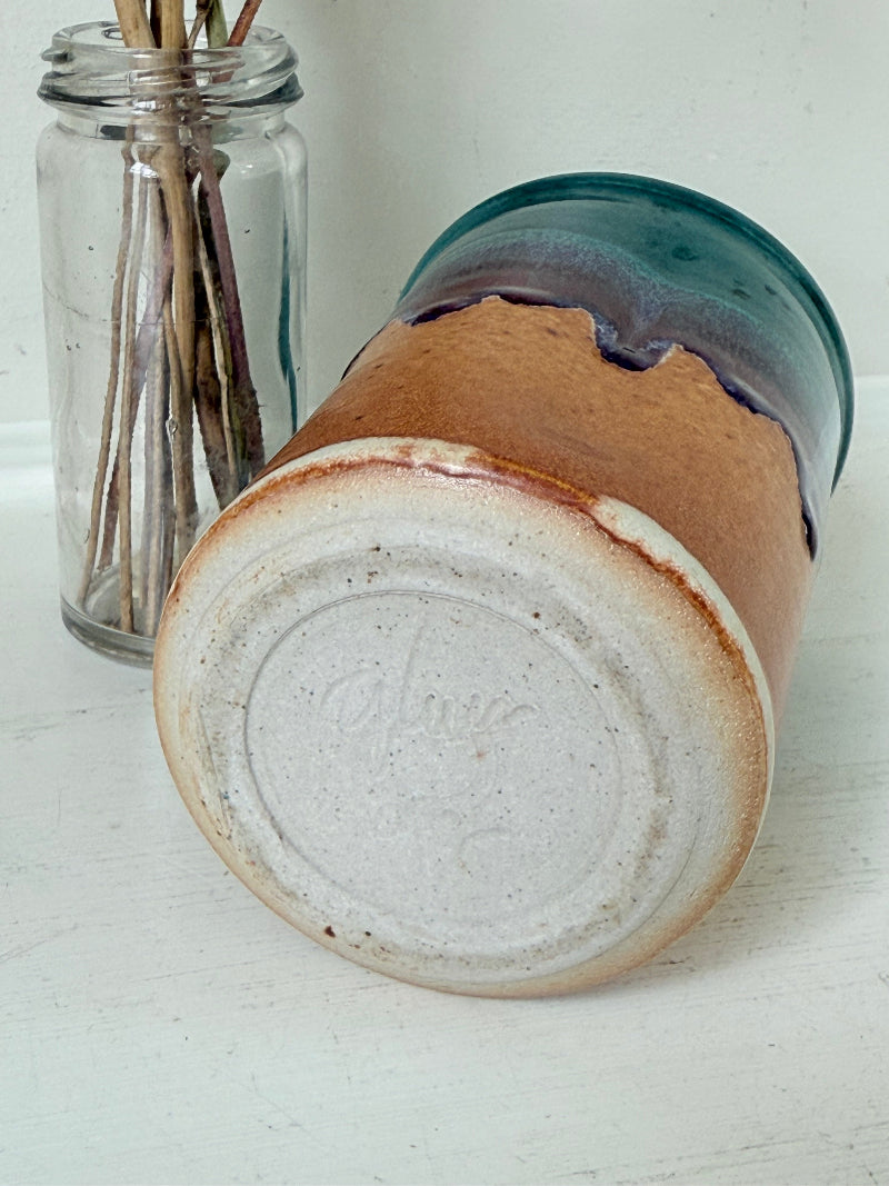 Studio pottery pen pot with teal and plum drip glaze, photographed on a white surface