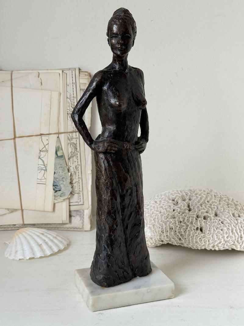 Solid bronze figure of a standing semi nude woman with upswept hair on a white marble base