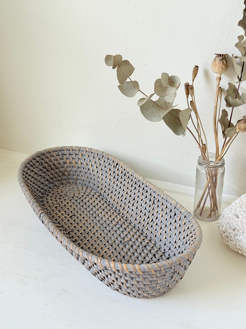 Vintage grey woven bread basket with oval shape and raised rim, photographed on white surface.