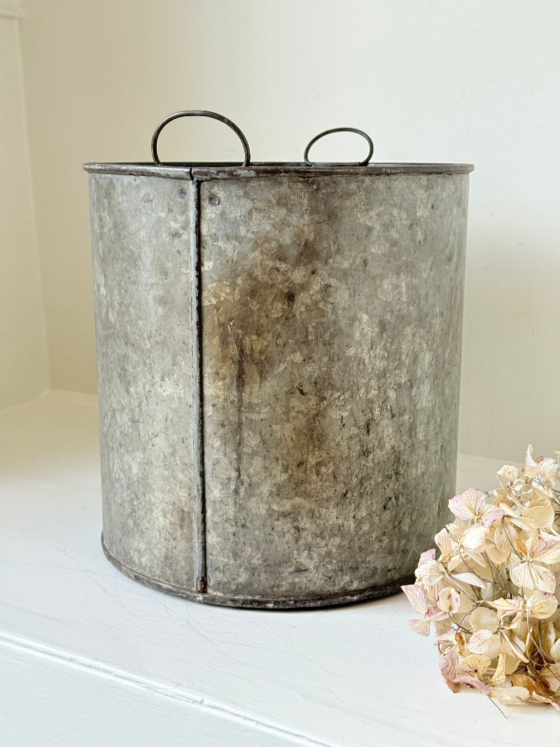 Vintage galvanised metal bin with handles, photographed on a white surface.