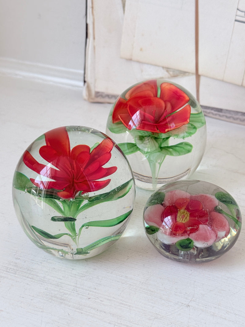 Trio of vintage glass paperweights with hand worked red floral detail, clear glass domes and green leaf decoration