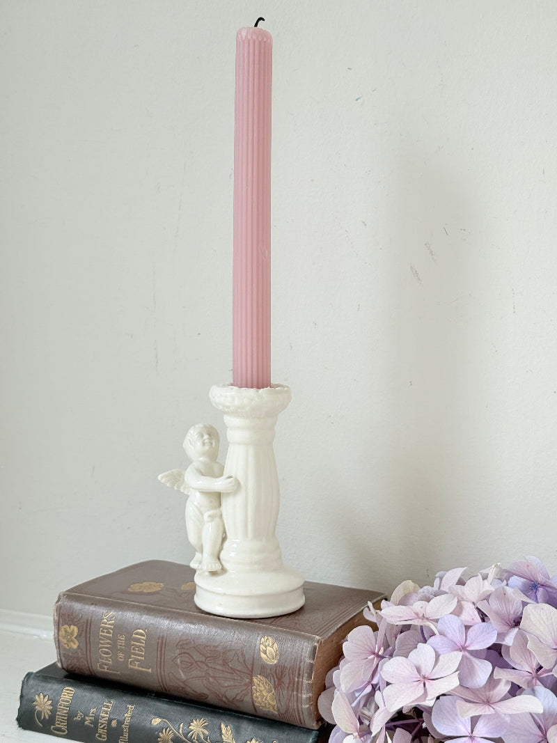 Vintage ceramic candlestick with angel figure and fluted column, cream glazed, styled with pink candle on white surface
