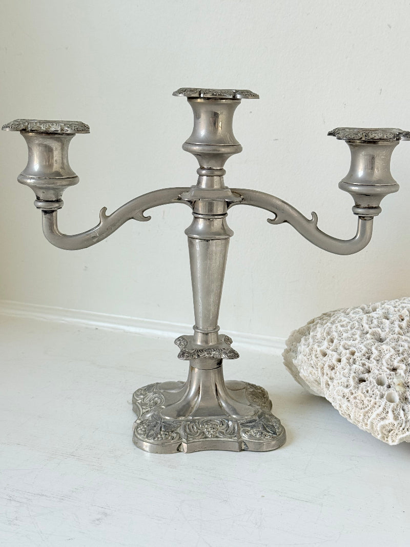 Vintage silver coloured three-arm candelabra with ornate base and soft patina, photographed on a white surface