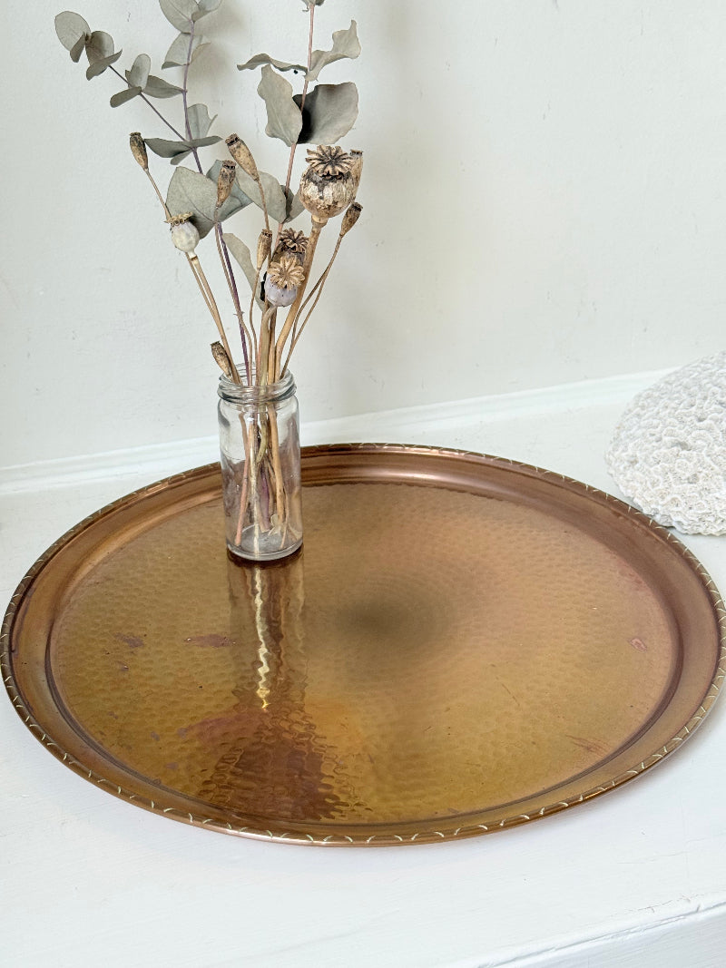 Lakeland Borrowdale hammered copper tray with warm patina, photographed on a white surface beside dried stems.