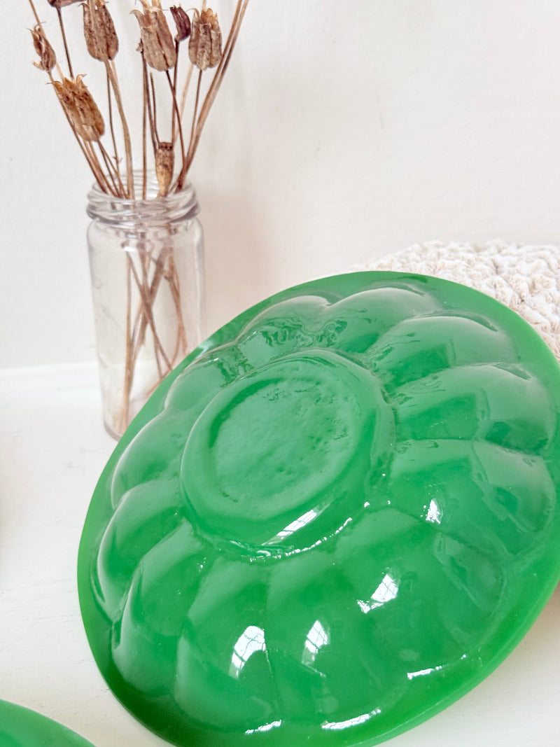 set of five vintage green pressed glass plates with decorative pattern, photographed on a white surface with dried flowers