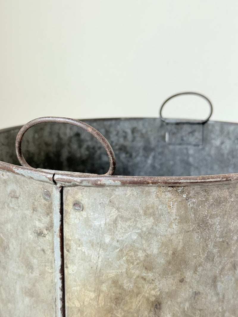 Vintage galvanised metal bin with handles, photographed on a white surface.