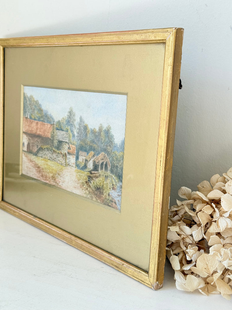 Framed vintage watercolour of countryside farm buildings with red roofs in gold frame photographed on a white surface