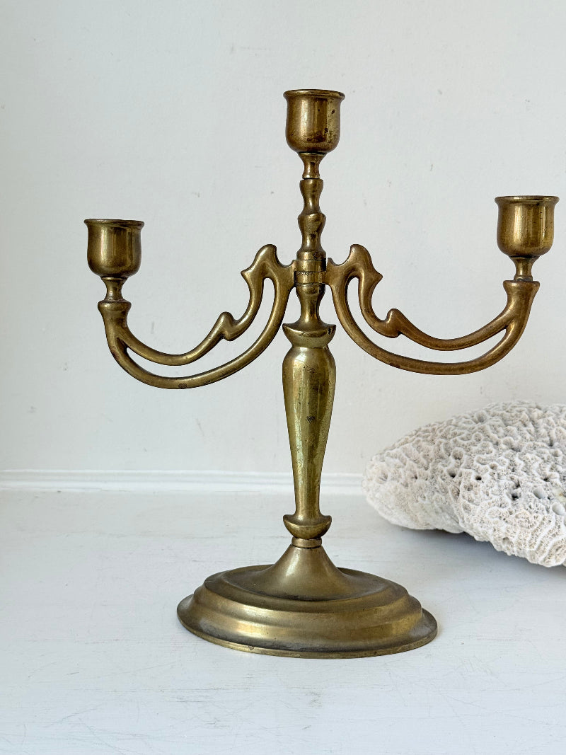Vintage brass three-arm candelabra with curved arms and soft patina, photographed on a white surface