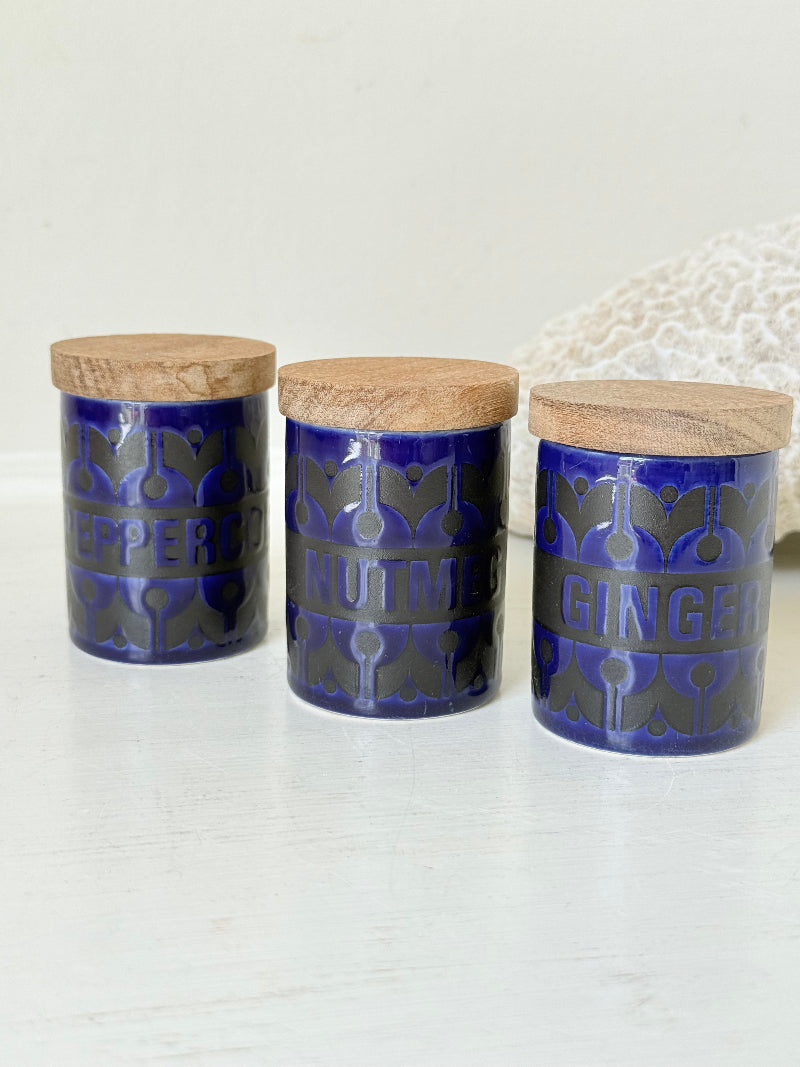 Set of three Hornsea Pottery spice jars in cobalt blue with wooden lids, labelled Ginger, Nutmeg, and Peppercorn, photographed on white surface