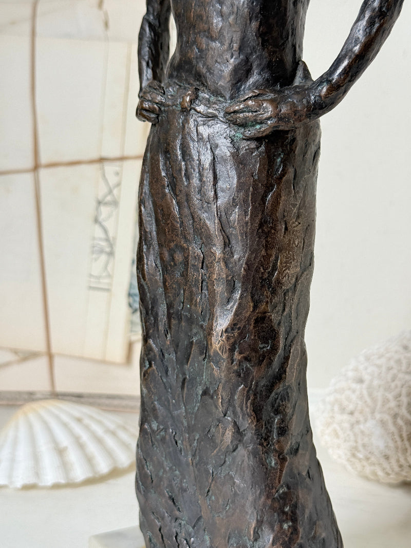 Solid bronze figure of a standing semi nude woman with upswept hair on a white marble base