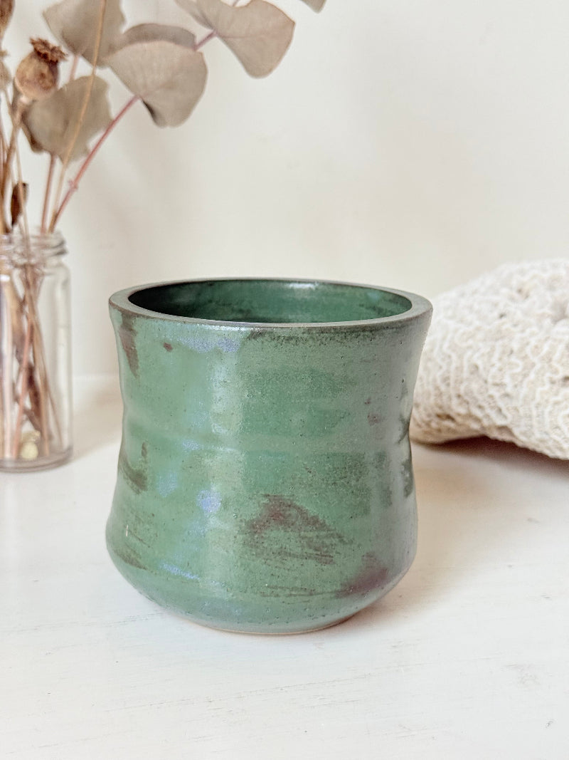 Studio pottery pencil pot in green glaze, handmade on the wheel, photographed on a white surface with pencils inside.