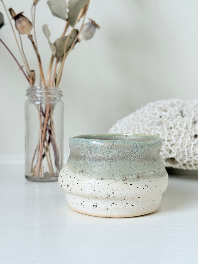 Studio pottery olive pot with soft green and cream glaze, photographed on a white surface