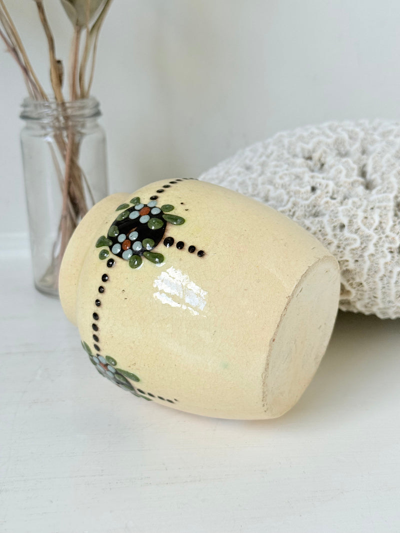 Cream studio pottery decorative pot with raised green floral motif, photographed on a white surface
