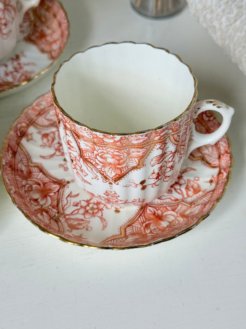 Vintage coral transferware coffee cans and saucers with scalloped edges and gold accents, set of ten, styled on a white surface.