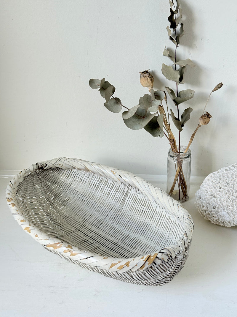 Vintage white chippy wicker basket with oval shape and worn painted finish, photographed on white surface.