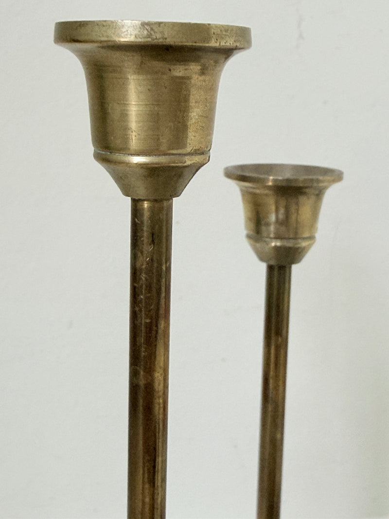 Set of 7 vintage brass candlesticks in graduated heights with aged brass finish styled with red ribbon on white surface