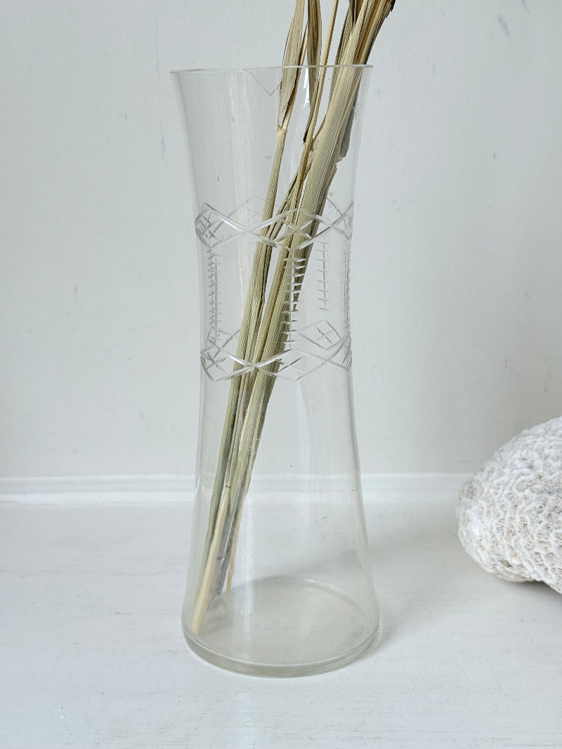 Vintage clear glass cylinder vase with etched leaf design, photographed on a white surface.