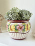 Large European hand painted floral ceramic jardinière with yellow, pink and green flowers on a white base, styled on a white surface with dried foliage.