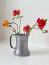 vintage pewter tankard with crown and rose mark and handle, styled with red and orange flowers on white surface