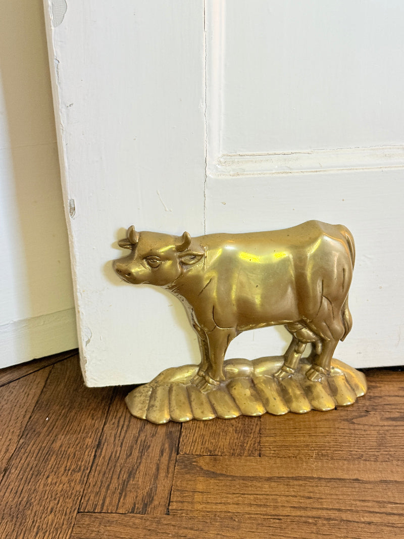 A small metallic gold bull figurine standing on a wave-like base, photographed on a wooden floor against a white door.