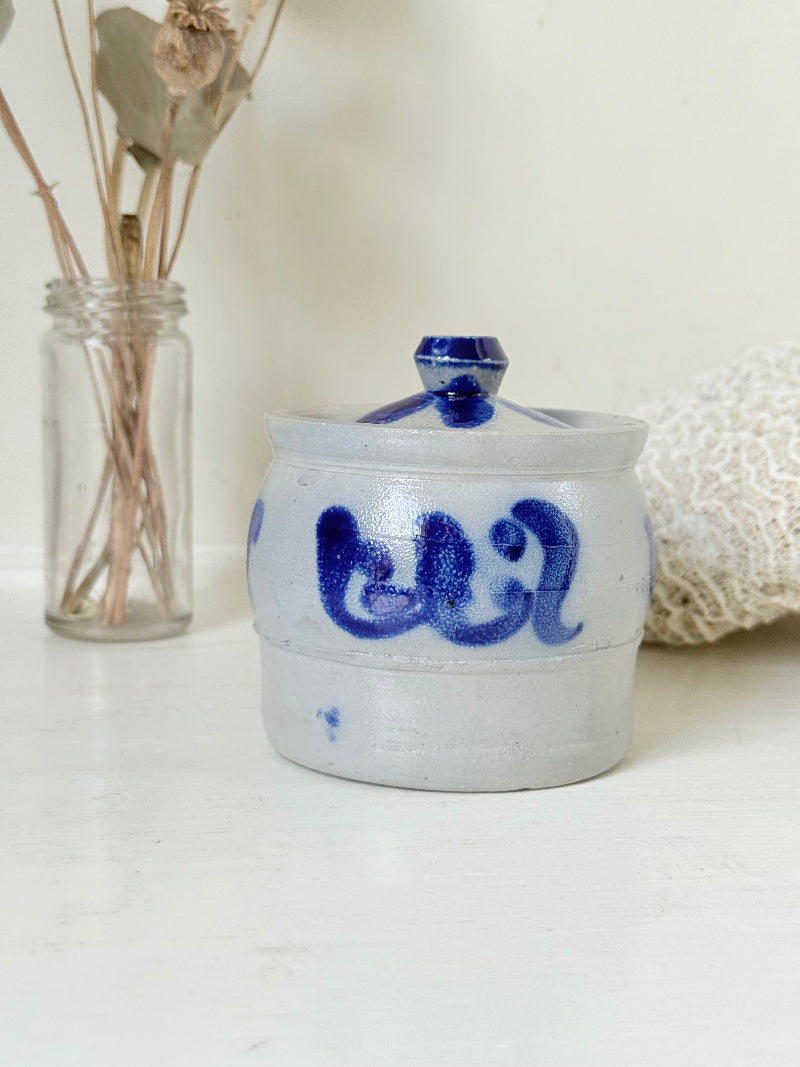 Vintage lidded pottery jar with hand painted blue floral decoration, photographed on a white surface