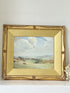 Framed oil painting of a rolling countryside landscape under a dramatic cloud-filled sky in an ornate gilt frame with wide mount.