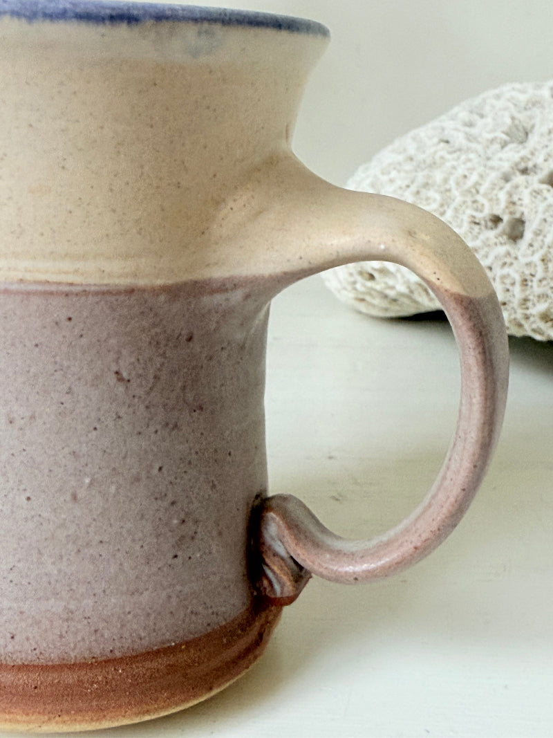Studio pottery milk jug in cream and lavender glaze with impressed initials, photographed on a white surface.