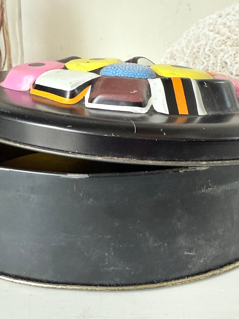 Vintage Liquorice Allsorts decorative tin with raised multicolour sweet design on black base, photographed on white surface.