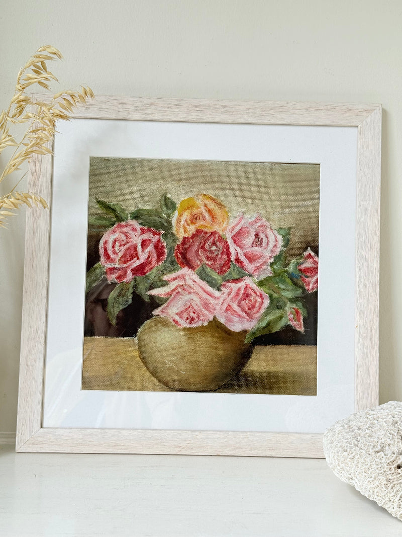 Framed original rose still life painting in pink and yellow, photographed on a white surface.