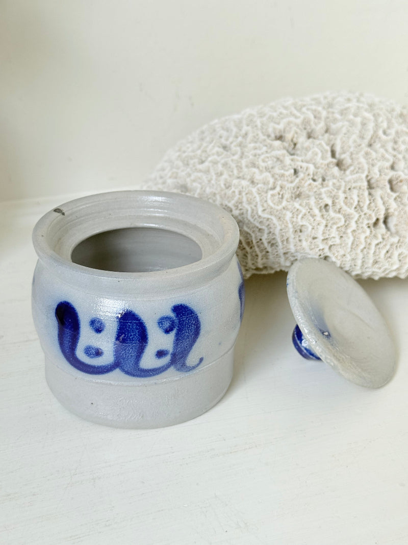 Vintage lidded pottery jar with hand painted blue floral decoration, photographed on a white surface