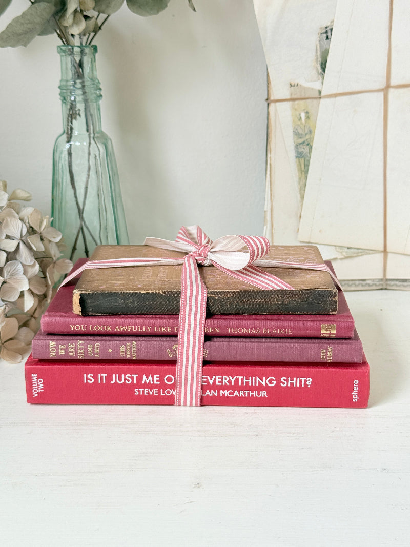 Stack of cloth bound vintage books in red and warm pink tones tied with striped ribbon and dried flowers