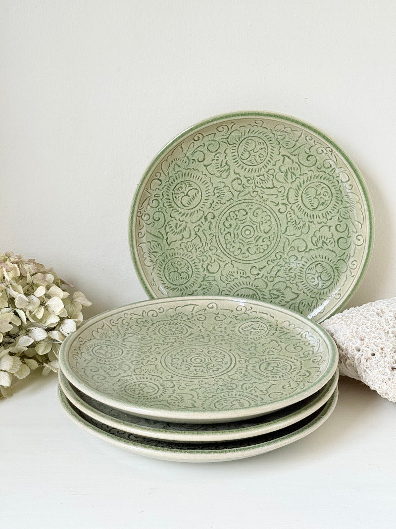 Set of four large Thai celadon stoneware plates in soft green glaze with raised pattern, photographed on a white surface