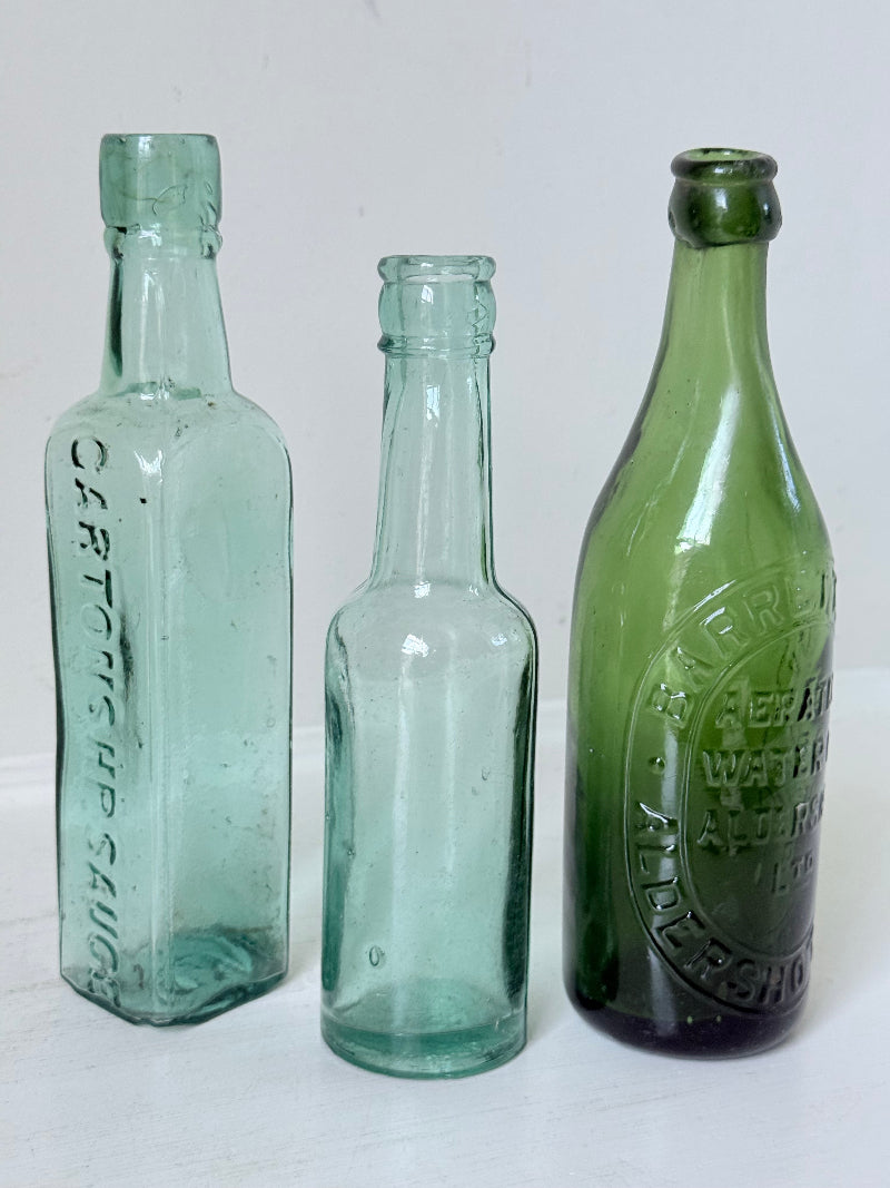 Trio of antique aqua and green glass bottles with embossed lettering, photographed on a white surface