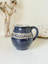 Studio pottery milk jug with deep blue glaze and cream geometric band, photographed on a white surface