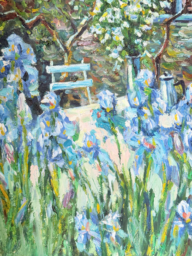 Framed impressionist-style oil painting of blue irises and garden scene, photographed on a white surface