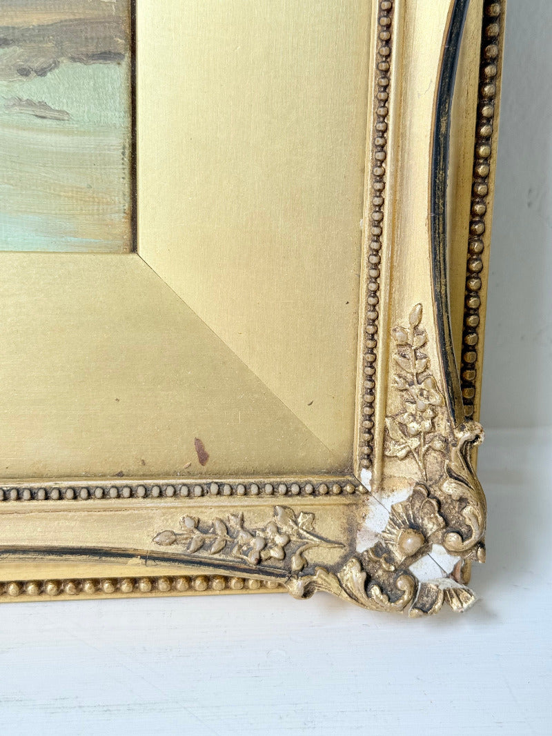 Framed oil painting of a rolling countryside landscape under a dramatic cloud-filled sky in an ornate gilt frame with wide mount.