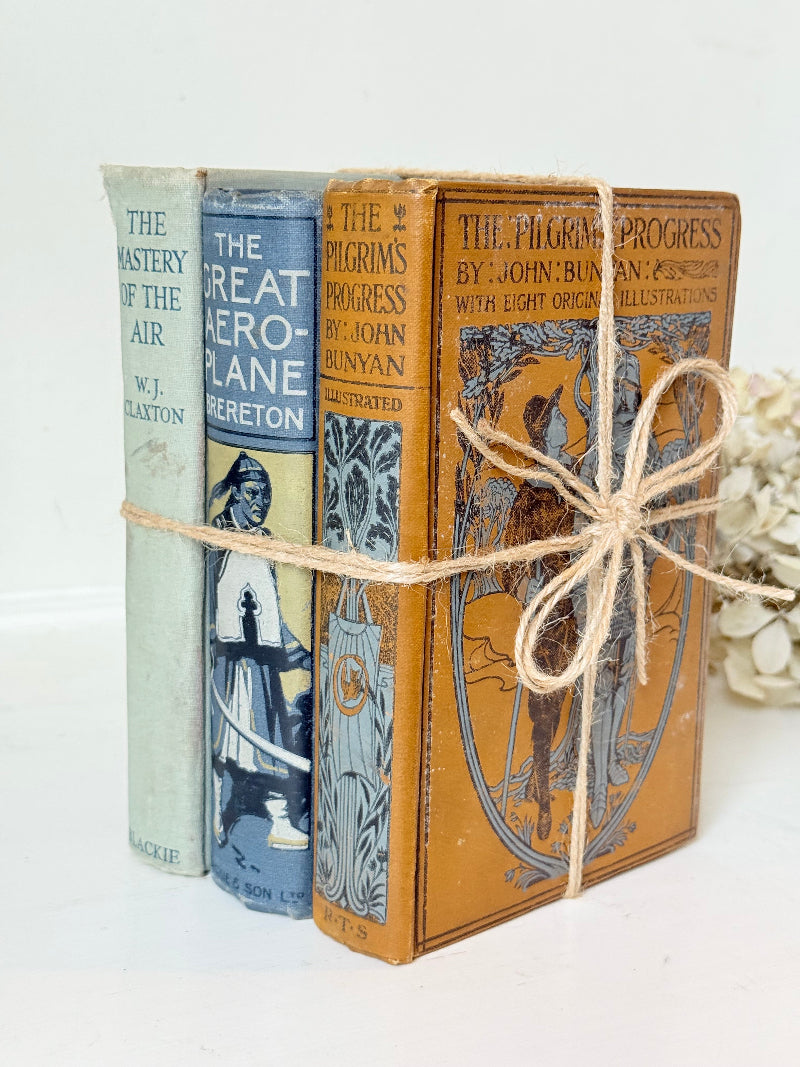 Vintage decorative book bundle in blue, grey, and ochre tied with twine, photographed on a white surface