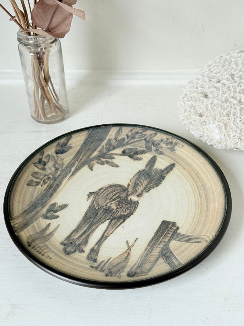 Vintage plate with hand painted brown donkey illustration and dark rim, photographed on a white surface