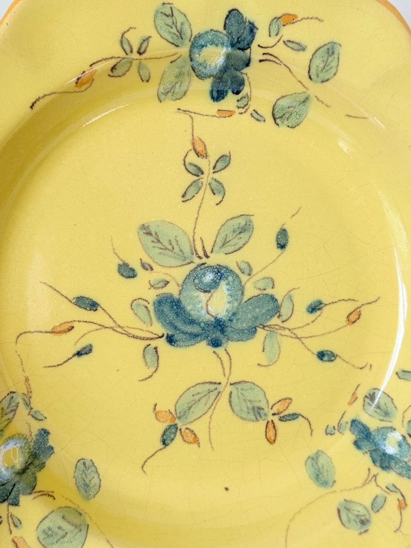 Vintage yellow French faïence plate with scalloped edge and blue floral decoration, photographed on a white surface