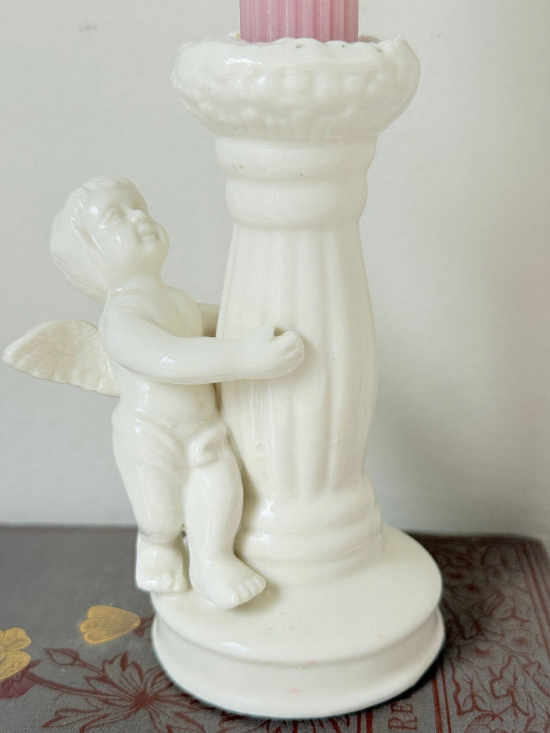 Vintage ceramic candlestick with angel figure and fluted column, cream glazed, styled with pink candle on white surface